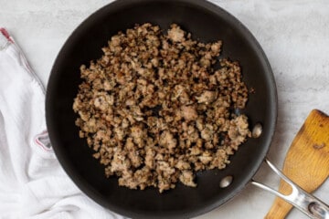 Browned sausage in skillet next to wooden spoon.