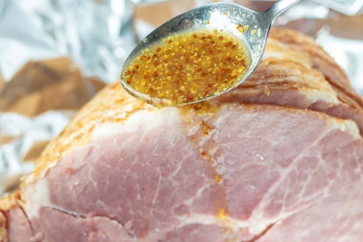 Spoon pouring pineapple mustard glaze over ham.