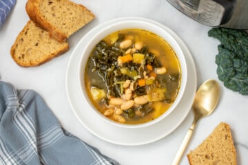 Bowl of Instant Pot White Bean and Kale Soup next to bread and pressure cooker.