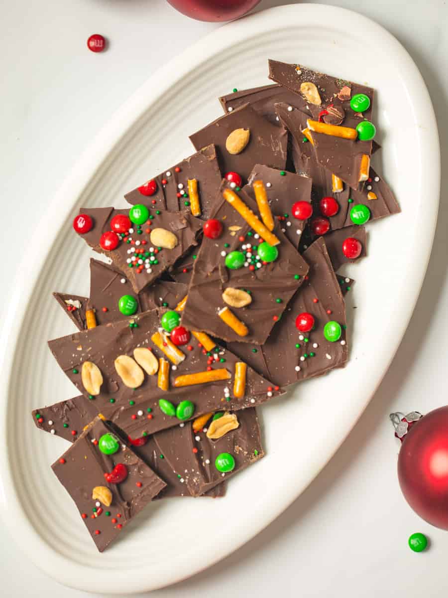 Plate of holiday chocolate bark topped with m&ms, pretzels, nuts, and sprinkles.
