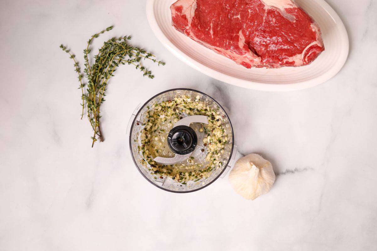 Mini food processor with thyme, garlic, olive oil, processed to form seasoning for steak.