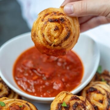 Pizza Roll-Up being held above pizza sauce for dipping.