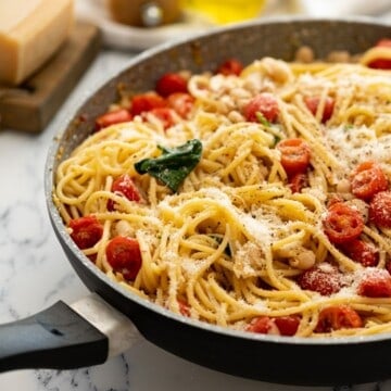 Large skillet with pasta, white beans, tomatoess, and spinach topped with parmesan.