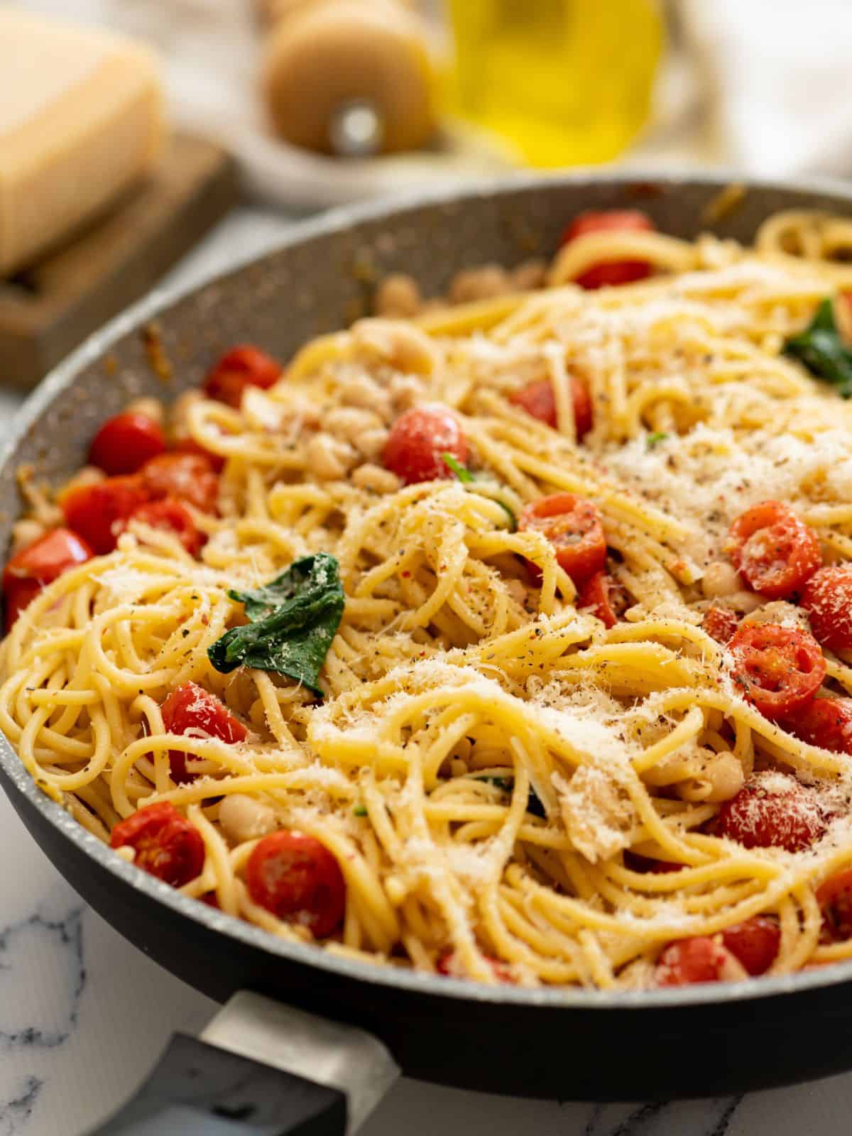 Large skillet with pasta, white beans, tomatoess, and spinach topped with parmesan.