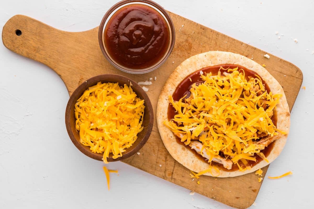 Assembled Pita Pizza topped BBQ sauce, cooked chicken and cheddar.