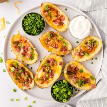 Baked Potato Skins topped with cheese, bacon, and green onions on platter.