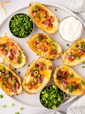 Baked Potato Skins topped with cheese, bacon, and green onions on platter.