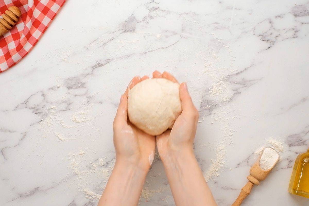 Hands holding pizza dough after being kneaded into a ball.