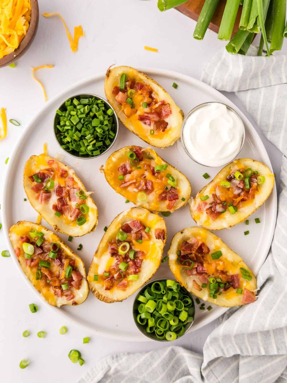 Loaded potato skins on white platter served with green onions and a dish of sour cream on the side.