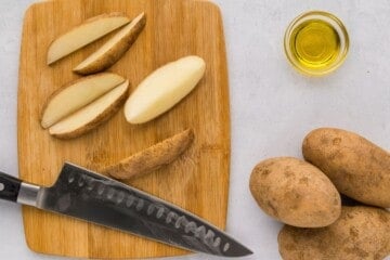 Russet potatoes cut into large wedges on wooden cutting board. O