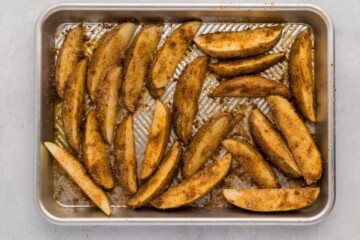 Potato wedges on baking sheet tossed with oil and seasonings.