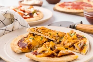 Baked BBQ Chicken Pita Pizza cut into 4 wedges on plate with other varieties of pita bread pizza in background.
