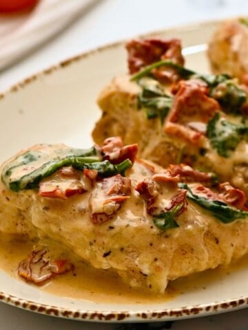 Instant Pot chicken breasts on platter topped with creamy parmesan sauce with sundried tomatoes.