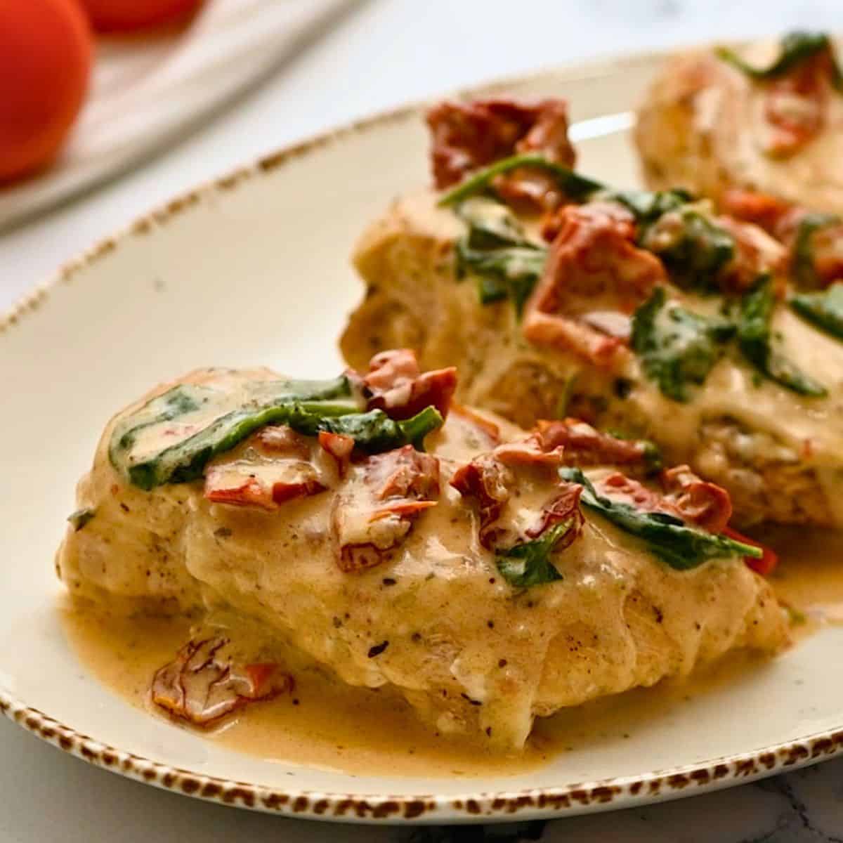 Instant Pot chicken breasts on platter topped with creamy parmesan sauce with sundried tomatoes.