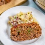 Slice of Instant Pot Meatloaf on white plate next to red smashed potatoes.