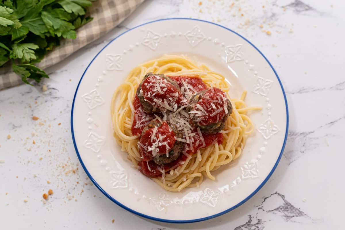 Baked meatballs serve on white plate with pasta, spaghetti sauce, and parmesan cheese.