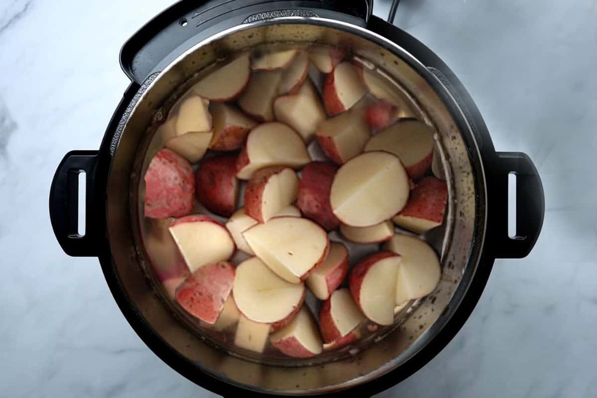 Red Potatoes with broth and salt inside inner pot of pressure cooker.
