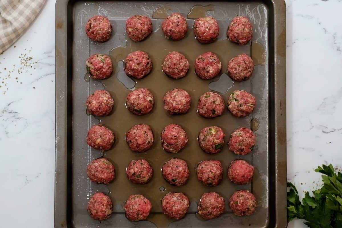 Shaped meatballs on baking sheet with a bit of beef broth.