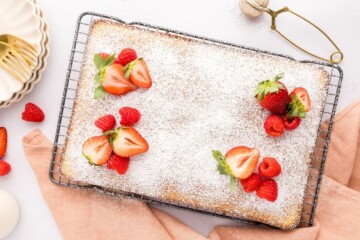 Hot Milk Sponge Vanilla cake dusted with powdered sugar and fresh fruit on cooling rack.
