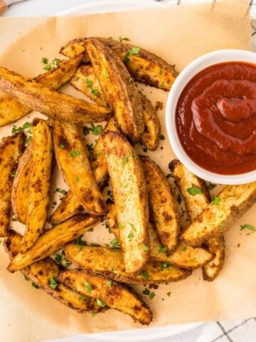 Baked Homemade Fries on parchment paper next to ketchup.