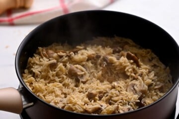 Tender rice and mushrooms in saucepan with steam coming out of pan.