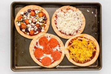 Four assembled pita pizzas on baking sheet.