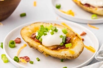 Crispy potato skin on white plate topped with sour cream, green onions, and bacon.