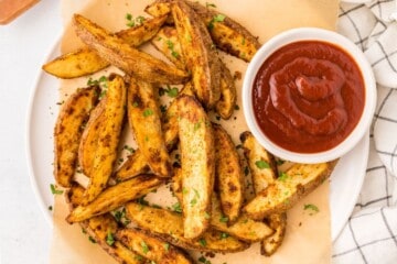 Baked Potato Wedges on parchment paper next to ketchup.