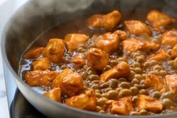 Skillet with orange chicken bubbling in sauce.