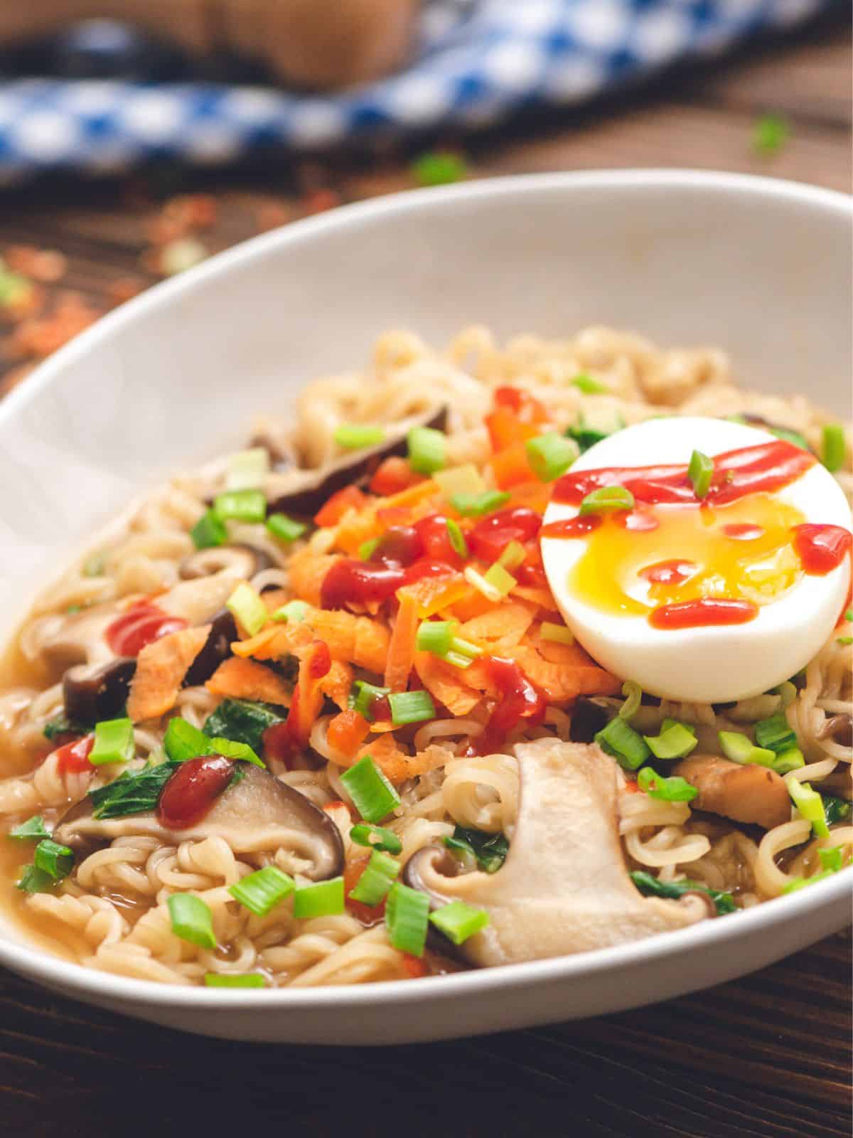 Bowl of homemade ramen topped with soft boiled egg, green onions, and sriracha.