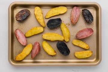 Halved fingerling potatoes tossed with garlic and olive oil and butter cut side up on rimmed sheet pan after halfway through baking.