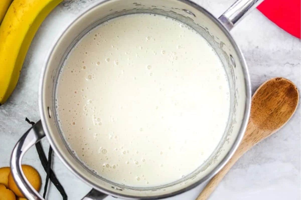 Vanilla pudding in saucepan next to vanilla wafers and bananas.
