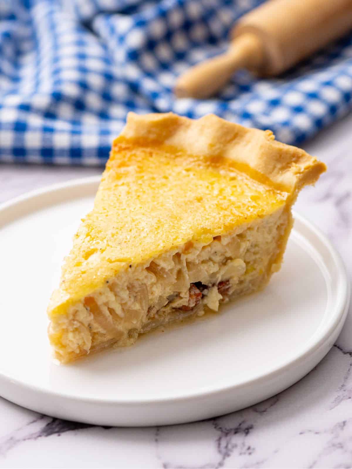 Slice of classic French Quiche Lorraine on white plate.