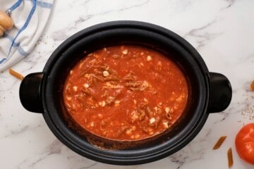 Cottage Cheese, pasta, and cheese in spaghetti sauce inside slow cooker.