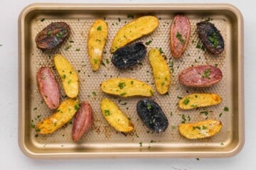 Fingerling potatoes tossed with garlic and olive oil and butter cut side down on rimmed sheet pan after roasting, topped with parmesan and parsley.