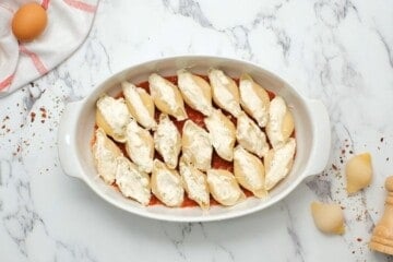 Stuffed cooked jumbo shells in baking dish lined with spaghetti sauce.