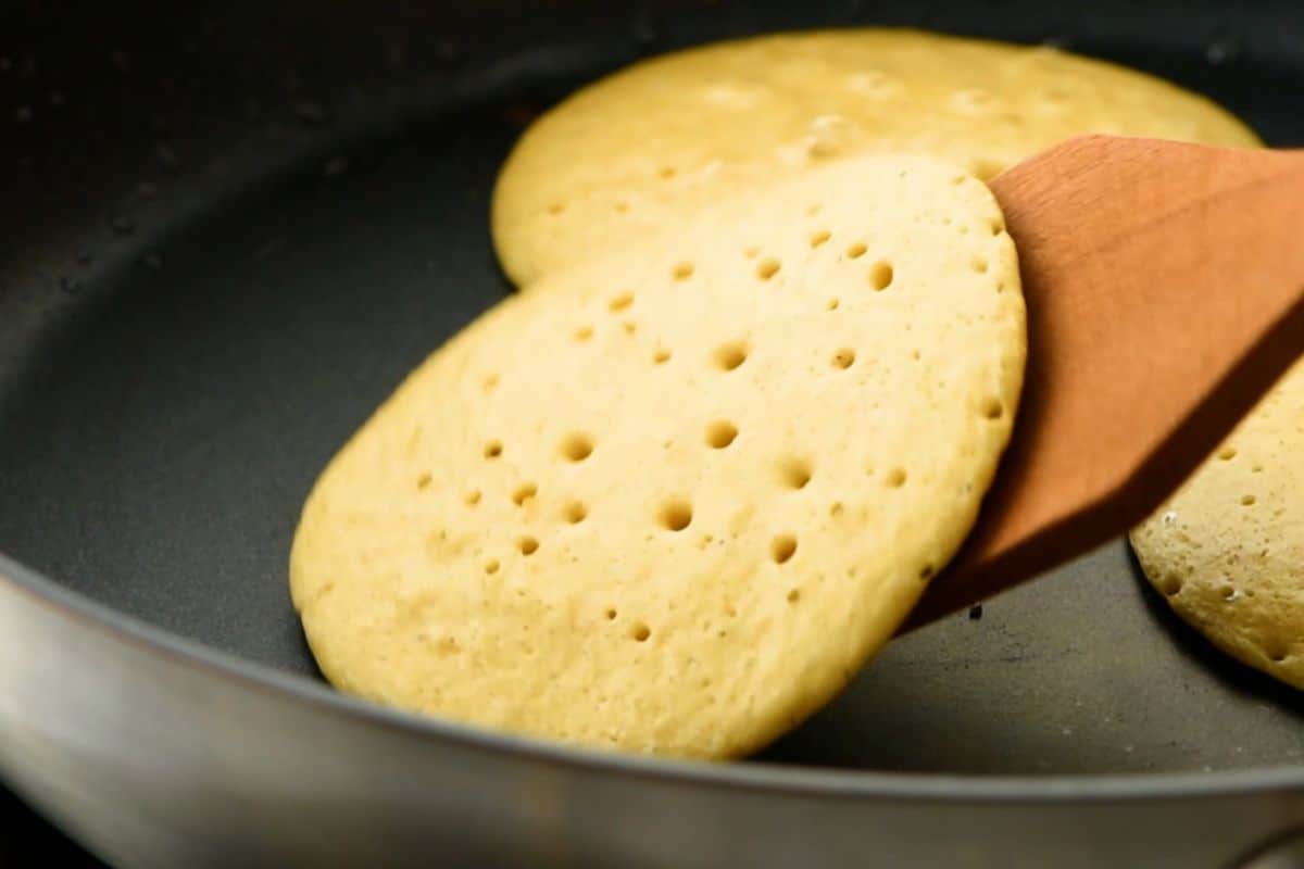 Oatmeal Pancakes being flipped over in skillet after small bubbles on surface formed.