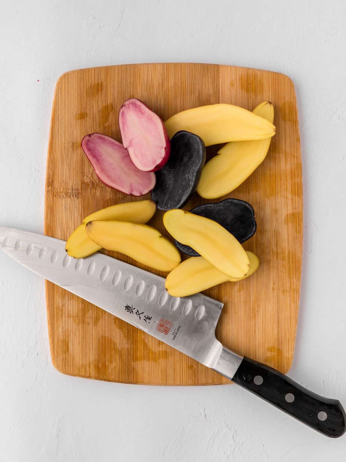 Fingerling potatoes cut in half on small cutting wooden cutting board next to knife.