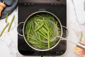 Slotted spider spoon taking green beans out of boiling water.