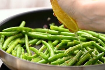 Lemon being squeezed over green beans in saute pan.