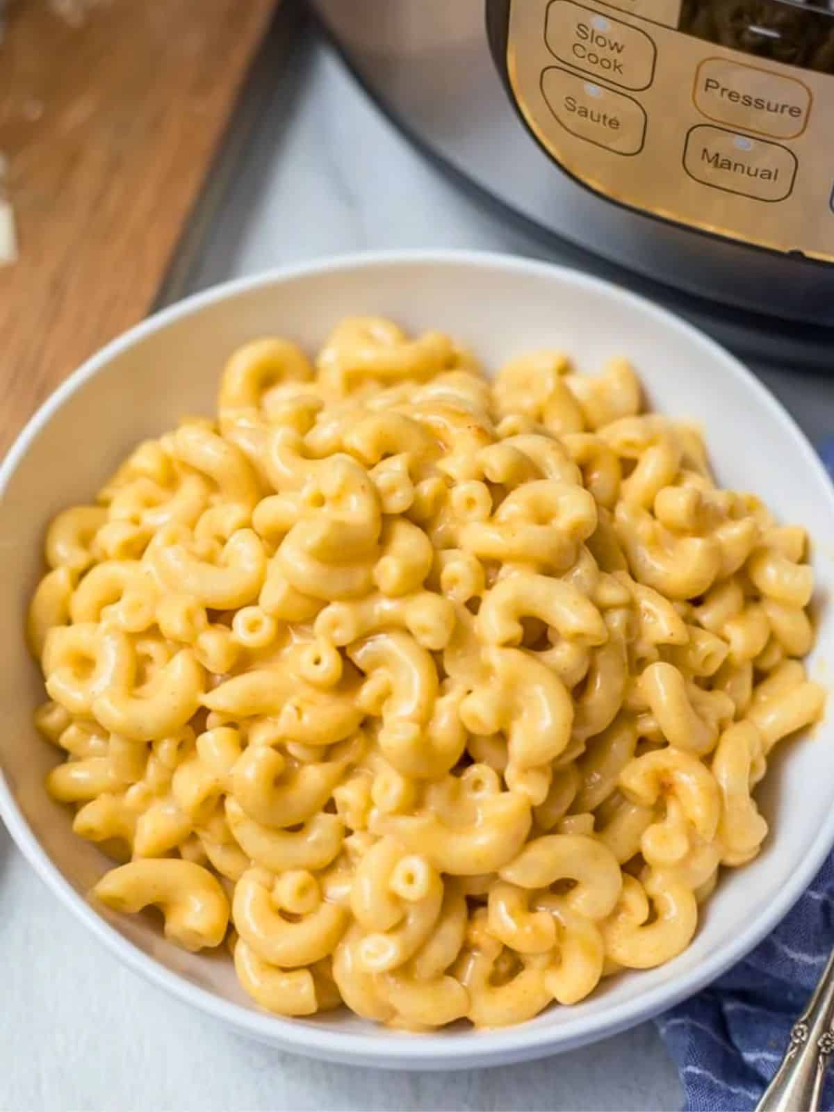Bowl of cheesy, creamy Instant Pot Macaroni and cheese next to pressure cooker.