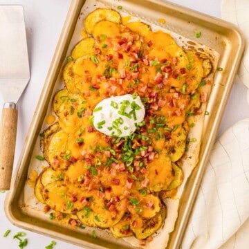 Loaded Irish Nachos on sheet pan topped with green onions and sour cream.