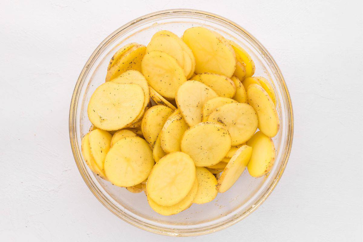 Thinly sliced potatoes in large mixing bowl tossed with salt, pepper, garlic powder, onion powder, and oil.