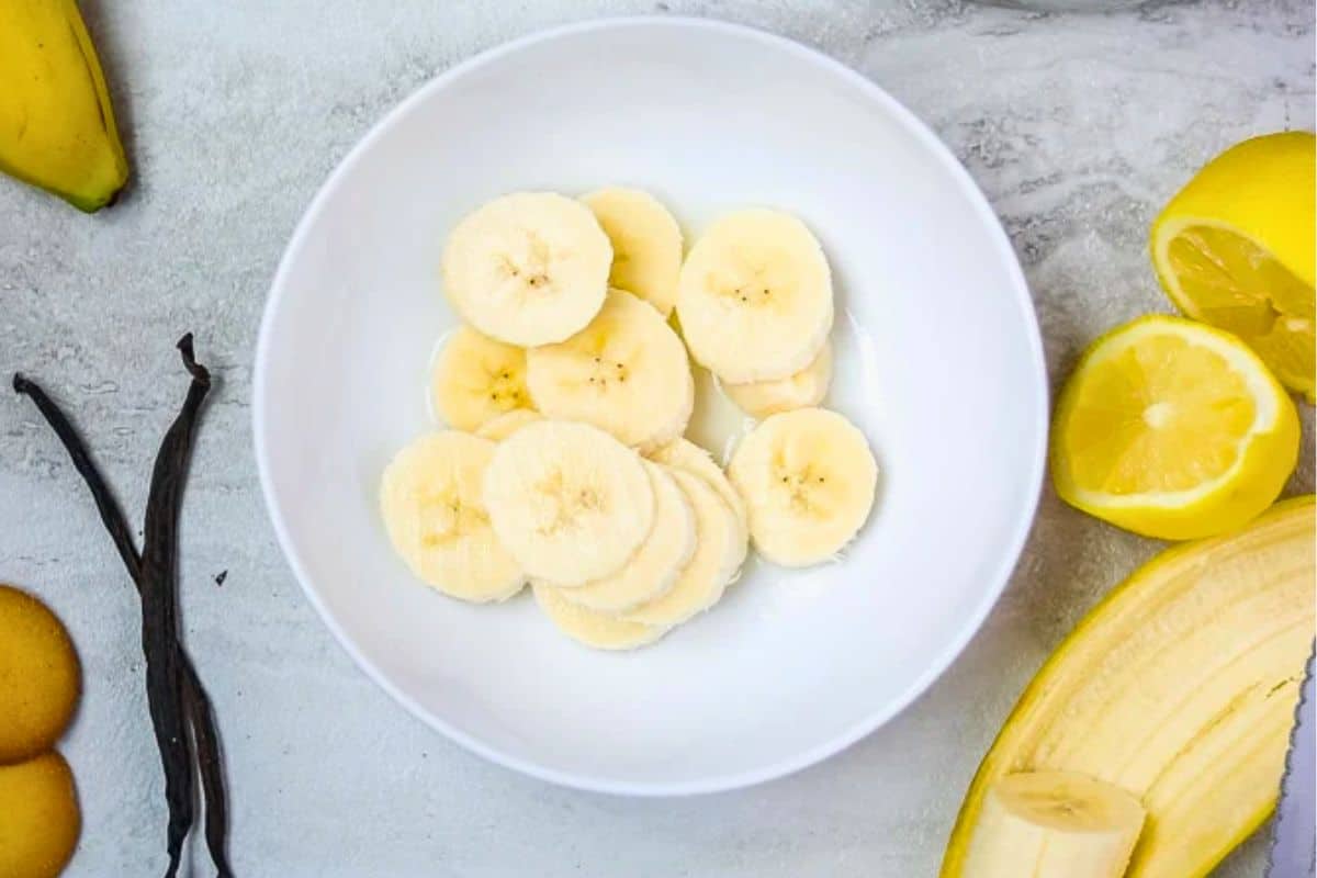 Sliced bananas in white bowl in lemon juice.
