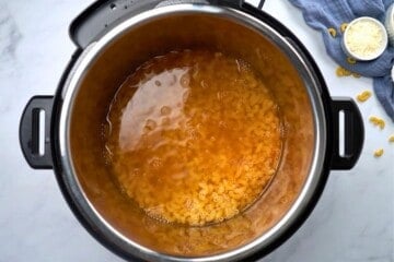 Elbow noodles with seasoned broth inside inner pot before pressure cooking.
