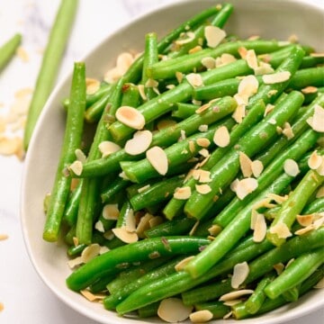 Bowl of green beans almondine topped with slivered almonds.
