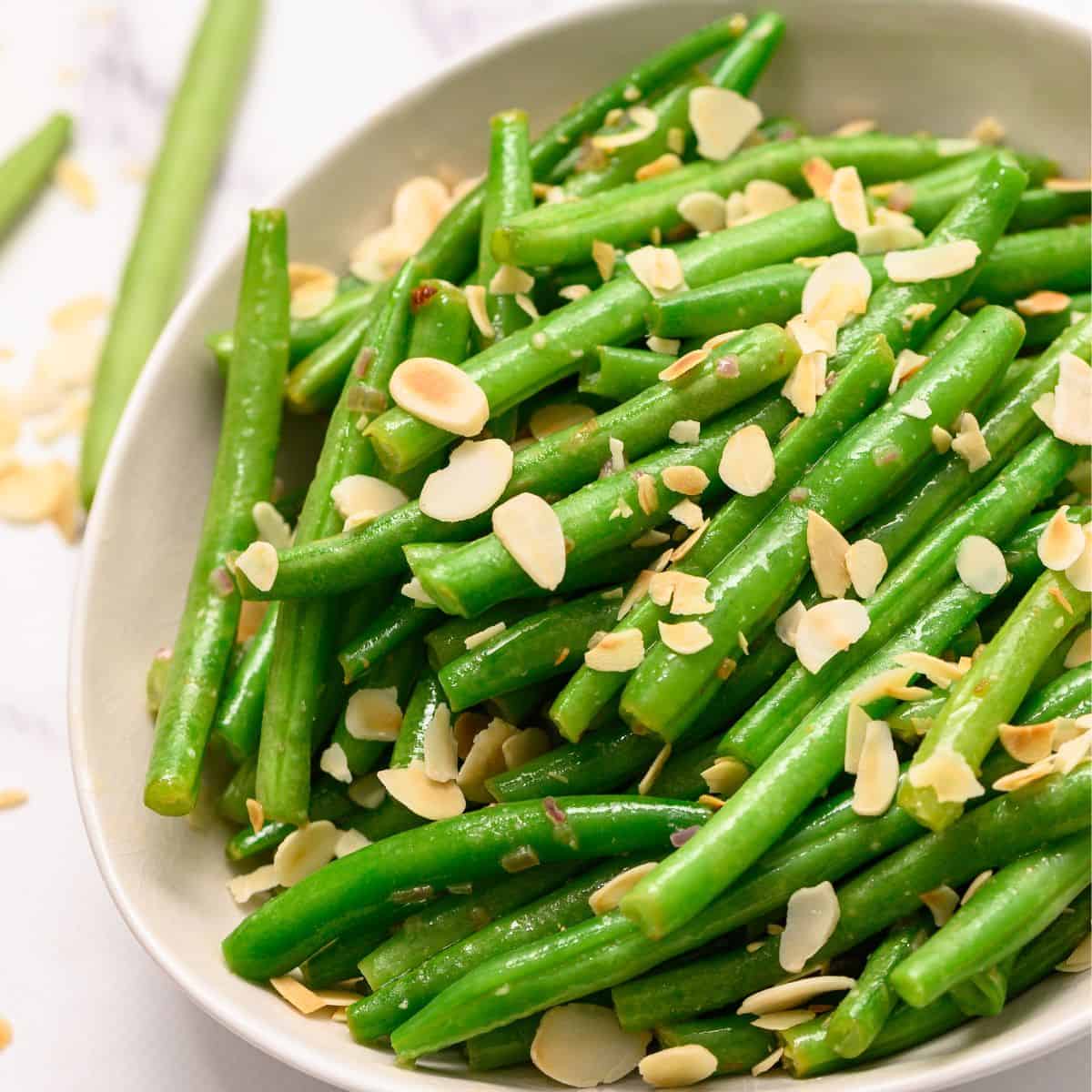 Sides for Holiday Dinner Bowl of green beans almondine topped with slivered almonds.