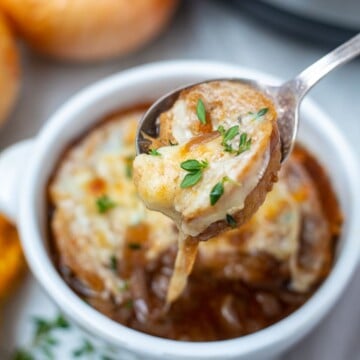 Spoonful of Instant Pot French Onion Soup with cheese pulling out of soup bowl.