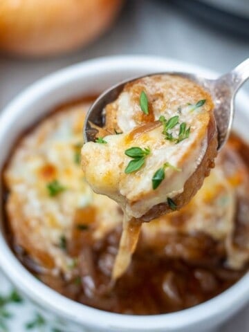 Spoonful of Instant Pot French Onion Soup with cheese pulling out of soup bowl.