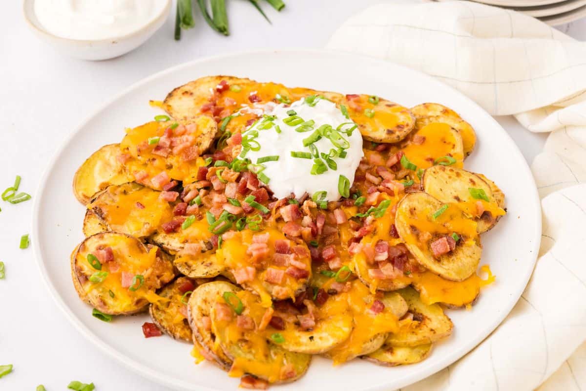 Loaded Irish Potato Nachos made with crispy baked potato slices topped with cheese and bacon served on white plate.